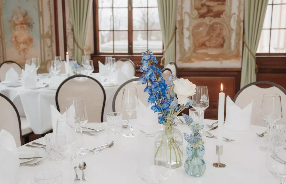 Elegant gedeckter runder Tisch mit blauen Blumen und Kerzen in einem Festsaal.