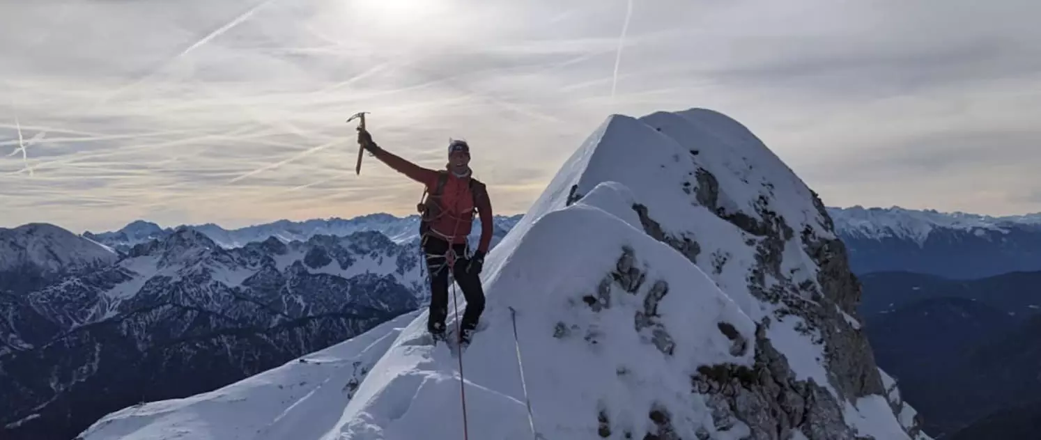 Bergsteiger auf winterlicher Alpen-Gratwanderung mit Eispickel, Panorama-Blick auf verschneite Berggipfel – alpines Klettern und Bergtouren in den Alpen