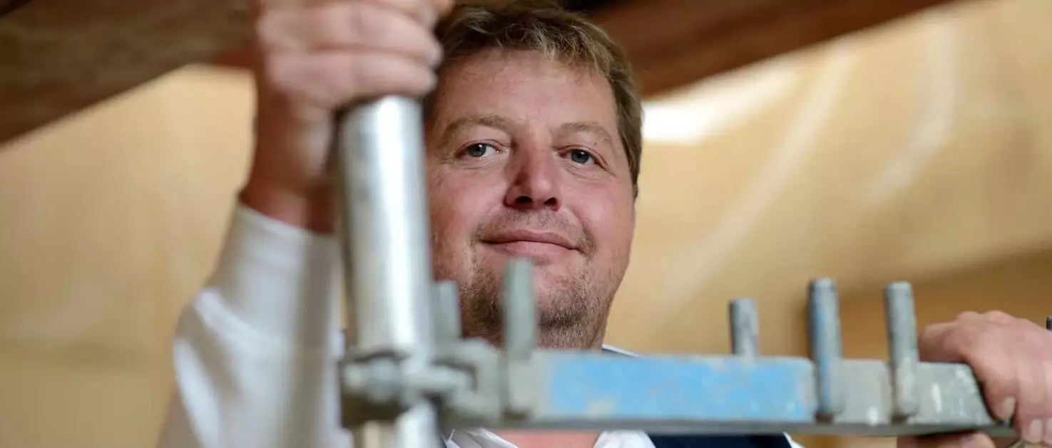 Lächelnder Handwerker mittleren Alters steht auf einem Metallgerüst und blickt direkt in die Kamera